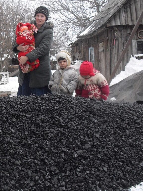 Mutter und 3 kleine Kindern stehen hinter einem Haufen Kohle