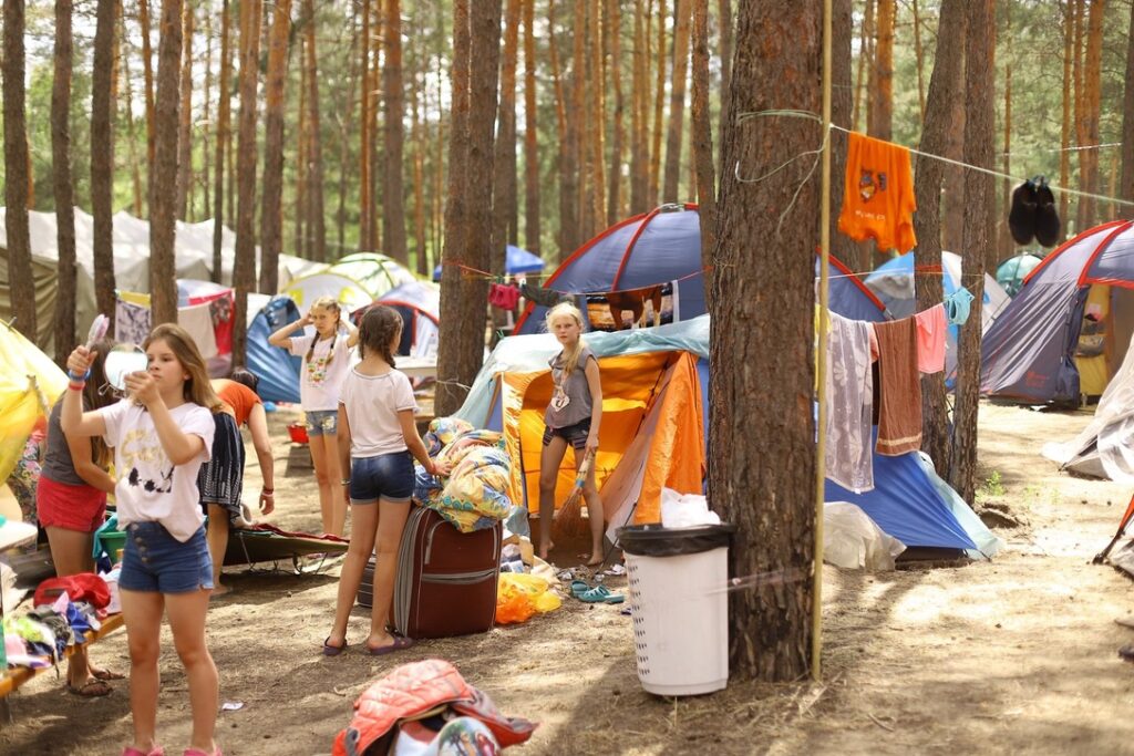Zeltdorf in einem Sommerlager; Zwischen den Stämmen von Bäumen sind Kinder, Zelte und Wäscheleinen
